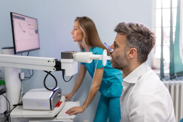 A man biting a sterile mouthpiece connected to a spirometer for a lung function test.